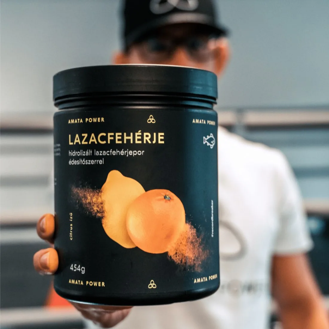 Sportoló a kamera felé tartja a citrus ízű Lazacfehérje dobozt